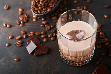 Glass of Irish cream baileys liqueur with roasted coffee beans, cinnamon and chocolate on dark wood background table. Selective focus.