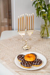 A lit Hanukkah with everyone on the festive table next to donuts and a vase of flowers.
