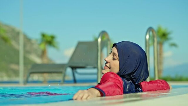 Young woman in a hijab swimsuit, cooling off by swimming in the pool, is enjoying her vacation. Slow motion video.Young woman wearing hijab swimsuit enjoying vacation.