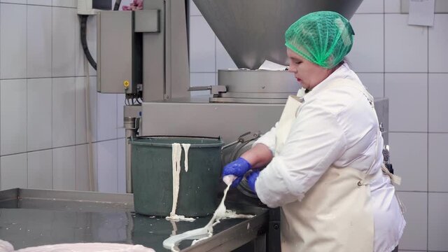 Side motion of female butcher processing sausages at meat factory. Adult woman wearing white coat and uniform making meat product in traditional way. Concept of food industry.