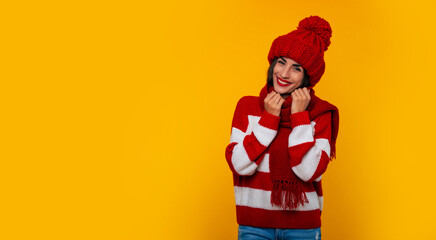 Close up photo of a beautiful happy brunette woman in red winter hat and scarf and posing isolated on yellow background