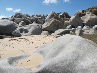 A wall of big boulders at the beach, against a blue sky. Curved-shaped gray boulder in the foreground. Virgin Gorda, British Virgin Islands, Caribbean.