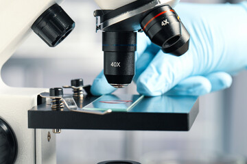 Scientist examining sample of red liquid on slide under microscope in laboratory, closeup