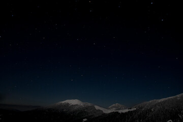 Naklejka premium Dark night starry sky over mountain top covered with snow.