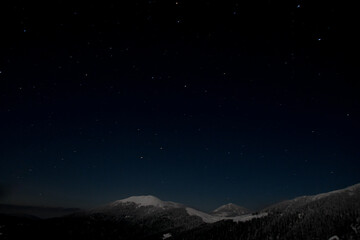 Dark night starry sky over mountain top covered with snow.