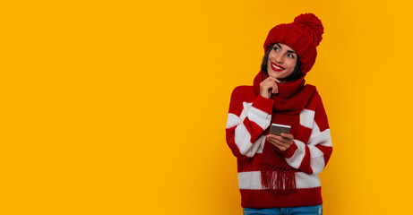 Portrait of happy and excited young modern beautiful woman in red winter hat and scarf while she uses her smart phone and having fun