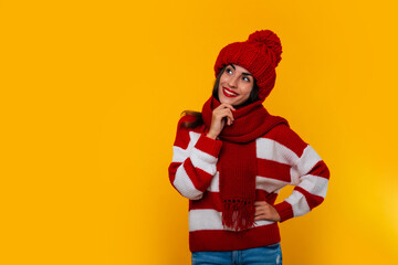 Close up photo of a beautiful happy brunette woman in red winter hat and scarf and posing isolated on yellow background