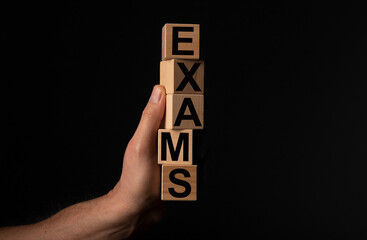 Exams word on wood dices in hand over black background with copy space.