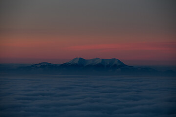 aerial view of evening sky with clouds and mountain tops covered with white snow.