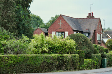 Red brick house with white shutters on the windows and surrounded by bushes and trees, England, UK