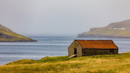 Fototapeta na wymiar Europe, Faroe Islands. View of sheep shelter on a grassy meadow overlooking the village of Eidi on the island of Eysturoy.