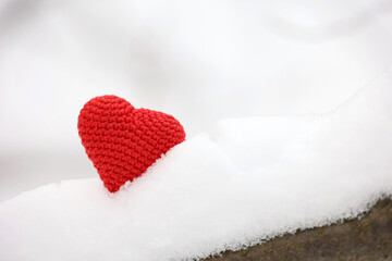 Fototapeta premium Knitted red heart in the snow in winter forest. Valentine's card, symbols of love, background for Christmas celebration