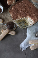 Tiramisu cake in a crystal square large plate on the table with a spruce towel and spoons. Dessert with mascarpone and savoyardi cookies.