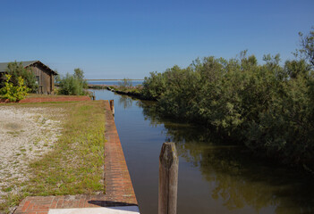 Obraz premium Landscape of the Venetian lagoon. View on a canal with bricole and the red brick wall, bushes and a wooden shed. Millecampi Valley, Italy.