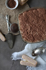Tiramisu cake in a crystal square large plate on the table with a spruce towel and spoons. Dessert with mascarpone and savoyardi cookies.