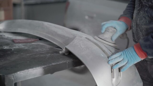 sanding car bumper with machine, in car repair shop