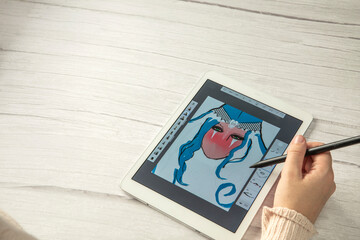 Young creative designer holding stylus pen drawing on screen of digital tablet on wooden desk with...