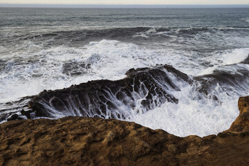 Cold waters of the Pacific churn and the salt water drains and cascades down coastal rocks