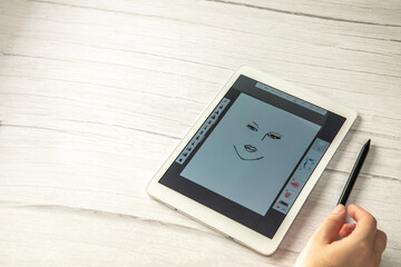 Young creative designer holding stylus pen drawing on screen of digital tablet on wooden desk with...