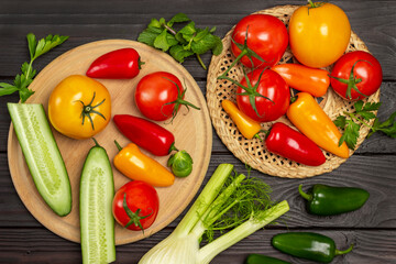 Chopped cucumbers and tomatoes on round board. Multi-colored peppers and tomatoes on wicker plate.