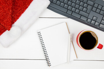 Notepad, computer keyboard, coffee and Santa hat on white table