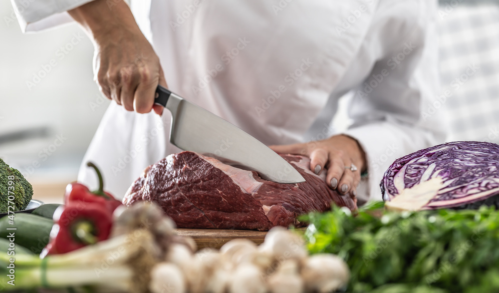 Wall mural chunk of pork meat cut with a sharp knife by professional chef with plenty of veg around