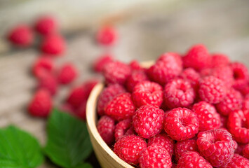 Fresh ripe red raspberries with leaves in a bowl on rustic old wooden table. Healthy organic food, summer vitamins, BIO viands, natural background. Copy space for your advertising text message.