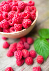 Fresh ripe red raspberries with leaves in a bowl on rustic old wooden table. Healthy organic food, summer vitamins, BIO viands, natural background. Copy space for your advertising text message.