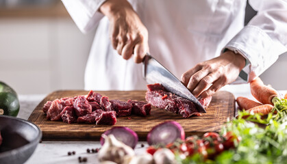 Chef cutting red meat to small chunks to prepare stew or goulash