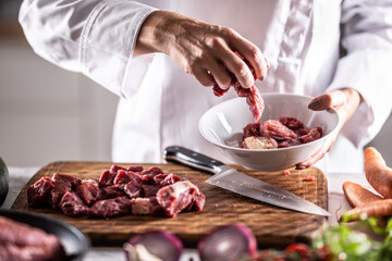 Chef puts pieces of pork into a bowl to cook it