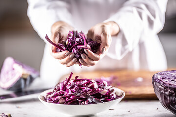 Thinly sliced raw red cabbage in hands and inside the bowl of a professional chef