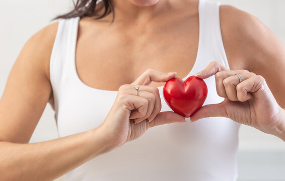 Woman holds small red heart over her chest in the area where the real heart is as a symbol of heart diseases prevention