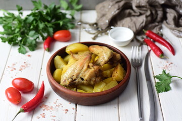 A hearty lunch for the family: baked chicken wings with potatoes on a beautiful plate on a white table. Close-up