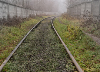 An old railway to a semi-abandoned closed facility in the autumn in the fog.