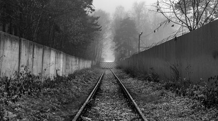 An old railway to a semi-abandoned closed facility in the autumn in the fog.