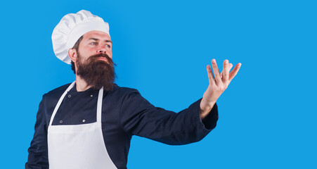 Bearded Male chef in uniform, apron and hat holds someting on hand. Copy space for advertising.