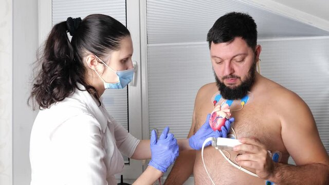 man patient with ECG cardiogram of heart, doctor cardiologist attaches sensors, examining and monitoring using holter equipment device for 24 hours daily monitoring of electrocardiogram, recorder