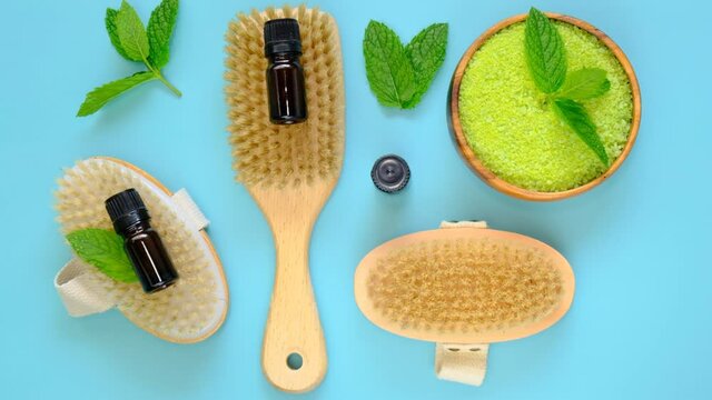 Essential mint oil and salt with mint extract, body brushes and fresh mint sprigs on bright blue background.Beauty and aromatherapy.Glass bottles with mint oil and sea green salt. 4k footage