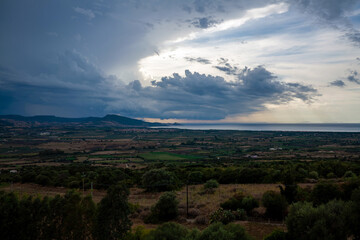 Fototapeta premium Dark storm clouds above a Mediterranean landscape inland, in the distance visible the sea.
