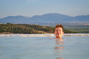 Pamukkale travertine in Turkey with man enjoying the views. Man traveler swimming at Pamukkale Natural Park and looking at beautiful sunset.Sexy young woman rest in Pamukkale 