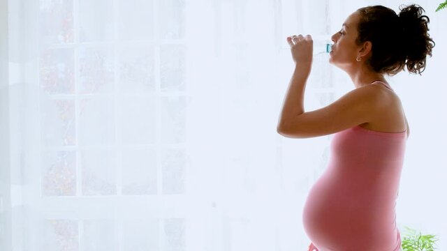 pregnant young woman drinking from a water bottle to hydrate after exercising. concept of health care and hydration in pregnancy