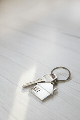 Silver key with silver house figure on white wooden background, buying new house real estate...