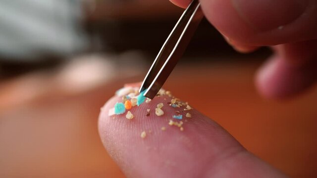 Global ocean pollution concept with microplastics bits and pieces from single-use plastic consumer items. Selective focus of a person examining micro plastics on his finger with a tweezers.