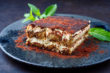 Modern style traditional Italian tiramisu served as close-up on a Nordic design gray plate on a black board
