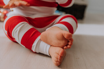 closeup of a baby's bare feet in Christmas striped pajamas sitting on a wooden floor. High quality photo