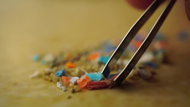 Global ocean pollution concept with microplastics bits and pieces from single-use plastic consumer items. Selective focus of a person examining micro plastics with tweezers.