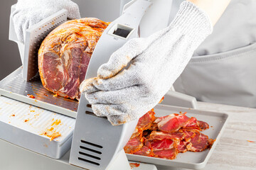 Close up isolated image showing a butcher or chef slicing a large frozen cured meat block. Turkish pastirma, pastrami, ham, beef concept. The person wears protective cut resistant gloves - obrazy, fototapety, plakaty