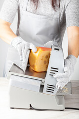 A chef is slicing a large chunk of swiss cheese using an electrical deli slicer. She wears protective cut resistant gloves while operating the machine.