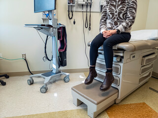 Inside of an  exam room with a bed, some medical devices, a computer. A woman is anxiously waiting for the doctor. Generic image for health care industry, disease, patient and doctor.