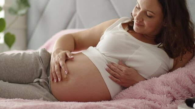 Happy pregnant woman expecting twins. Pregnant woman feeling happy at home while taking care of her child. Woman pregnancy concept and maternity prenatal care. Young expecting mother  Slow motion.